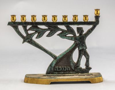 חנוכיית פליז, שרוליק. חנוכיית פליז ישראלית, מעוטרת בדמות שרוליק מחזיק ענף עץ זית. גובה: 17 ס"מ. 