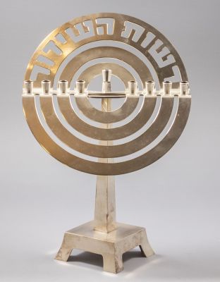 חנוכיית רשות השידור. חנוכיית מתכת מצופה-כסף עם סמל רשות השידור. גובה: 31 ס"מ.