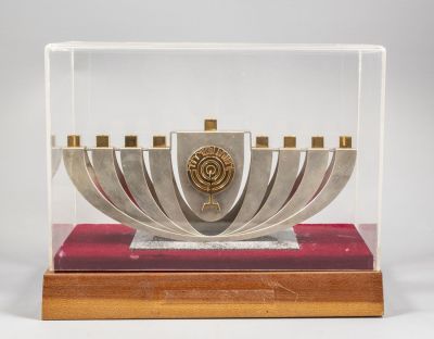חנוכיית רשות השידור מכסף סטרלינג, דגם לא שכיח. בזיכים וסמל הרשות מוזהבים. אורך: 28 ס"מ. משקל: 