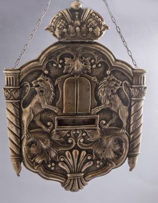 טס לספר תורה מצופה כסף. מעוטר בעבודת בלט במראה אריות אוחזים את לוחות הברית, כתר ומוטיבים 