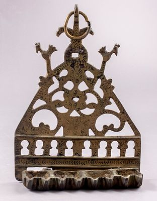 חנוכיית פליז סורית. חנוכיית פליז, ככל הנראה סוריה, המאה ה-19. גב מעוטר בעבודת חסר בדוגמת קשתות 