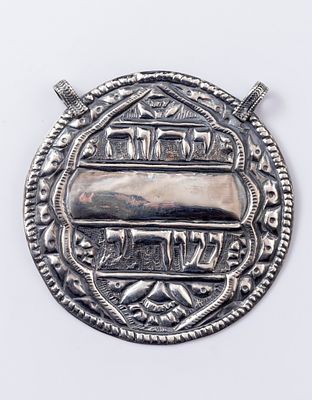 קמע כסף יהודי, מעוטר בשם המפורש ובכיתוב "שדי". קוטר: 7.5 ס"מ. משקל: 35 גרם. הכסף נבדק.