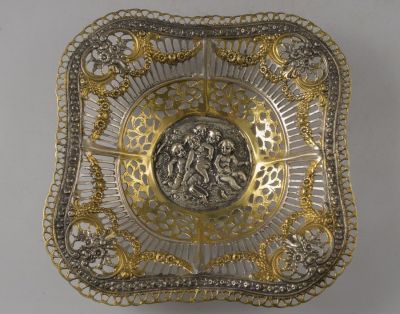 קערת כסף 800 בסגנון ניאו-קלאסי. מעוטרת בתבליט עם דמויות פוטי, בהזהבות ובעבודה פתוחה. 21.5X21.5 