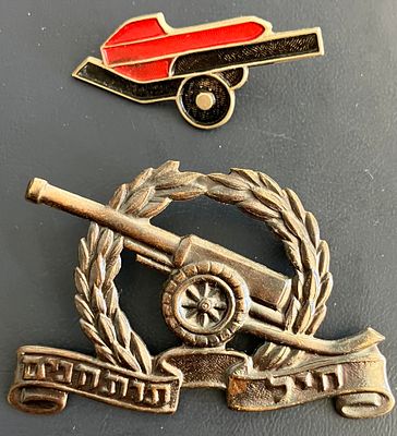 לוט 2 סמלים מוקדמים של חיל תותחנים : 
א. סיכת אות התותחן הישן; 
ב. סמל כומתה של החיל.