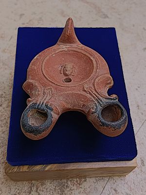 נר חרס . Lamp with two spouts, loop handle at rear, depicting theatrical mask; red slip; 11.9 x 