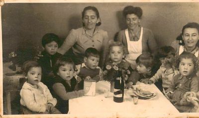 תצלום אחד, גודל הגלויה. גן ילדים בישראל של שנות השלושים, עם קופסת קק"ל על השולחן.