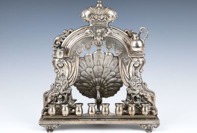 A LARGE PEACOCK SHAPED HANUKKAH LAMP. Austria, c. 1900. On four fancy feet. The backplate 