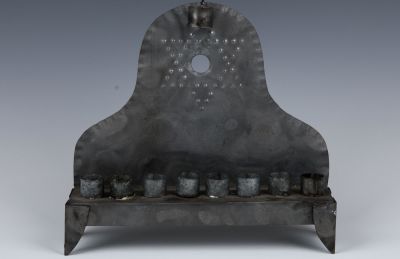 A TIN HANUKKAH LAMP. Probably American, c. 1900. On four feet. The backplate embossed with a 
