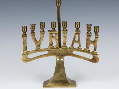 A BRASS IVRIAH MENORAH. American, c. 1940. On tapering rectangular base. With original servant 