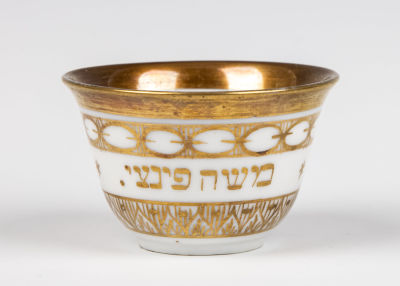 26. A PORCELAIN TEA CUP. Probably Germany, c. 1900. With the Hebrew name of Moshe Pinzi. 1.7” tall.