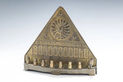 A BRASS BEZALEL HANUKKAH LAMP. Jerusalem, c. 1910. With a stylized shaped back and eight bullet 