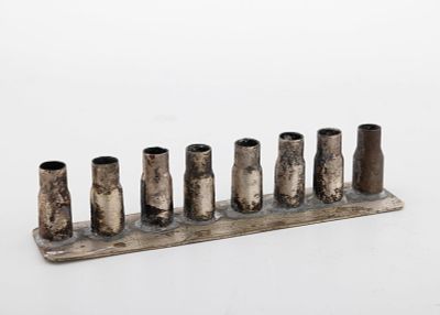 A TRENCH ART HANUKKAH LAMP. Palestine, c. 1920. Made of eight shell casings soldered onto a 