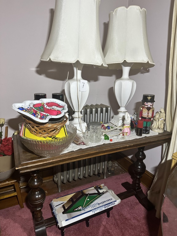 Table With Lamps & Contents wood table with turned legs, pair of white table lamps, glass bowl, basket, holiday plate, nutcracker, small fig