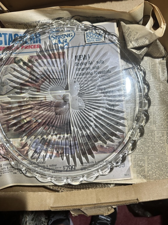Box Lot Of Glass Plates & Silverplate estate box lot with glass cake plates, trays, candlestick, and assorted serving pieces.
