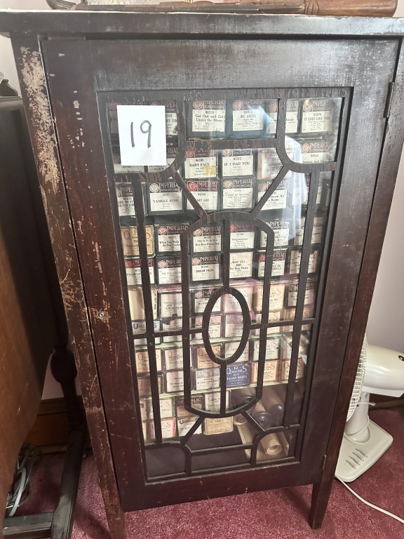 Cabinet With Player Piano Rolls wood cabinet with glass door and assorted player piano rolls.
