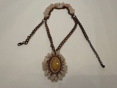 שרשרת מתכת בגוון ברונזה עם תליון אובלי גדול במרכז.