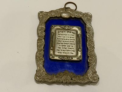 לוח קיר דקורטיבי המציג את “ברכת הבית” בעברית, יצוק בתבליט על גבי לוח מתכת קטן במרכז. הלוח משובץ 