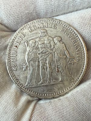 רפליקה של מטבע צרפתי קלאסי בעיצוב “Hercule”, שנת 1875. 
בצד אחד דמות הרקולס עם דמויות החירות 