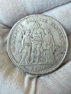 רפליקה של מטבע צרפתי קלאסי בעיצוב “Hercule”, שנת 1875. 
בצד אחד דמות הרקולס עם דמויות החירות 