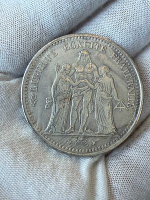 רפליקה של מטבע צרפתי קלאסי בעיצוב “Hercule”, שנת 1875. 
בצד אחד דמות הרקולס עם דמויות החירות 