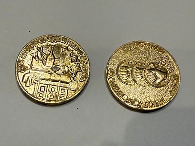 לוט הכולל שני אסימונים דקורטיביים בסגנון סובייטי, עם כיתוב ברוסית ועיצובי תעמולה אופייניים.