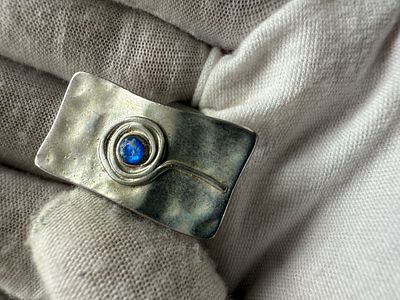 A modernist/artistic design ring, featuring a small blue cabochon-style stone set at the center 