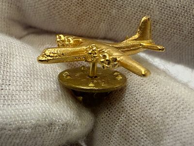 Gold-tone lapel pin in the shape of a C-130 Hercules aircraft. Marked BALLOU REG’D – 130 YEARS 