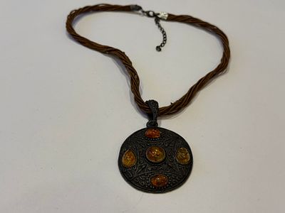 שרשרת חוטים מרובים בגוון חום טבעי, עם תליון עגול גדול בסגנון אתני/סקנדינבי. התליון עשוי מתכת 