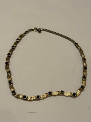 שרשרת חצי־קשיחה בעיצוב גלי ודקורטיבי, עשויה מתכת בגוון זהב מט (ייתכן פליז או סגסוגת מצופה). 
