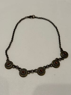 שרשרת מתכת בגוון ברונזה מושחרת, המורכבת מחמישה אלמנטים עגולים דמויי פרח/שמש. במרכז כל אלמנט 