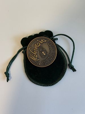 A decorative bronze-finish metal medallion housed in a dark green velvet drawstring pouch. The 
