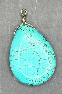 Turquoise-coloured teardrop cabochon pendant, wire-wrapped with a gold-tone bail. The stone 