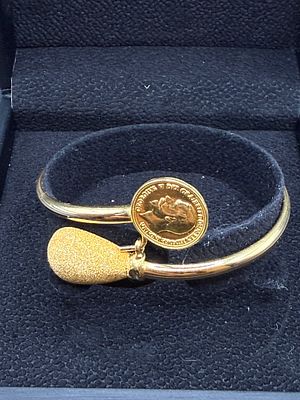 21K gold bypass/wraparound bangle bracelet. One end is set with a coin in the style of a 