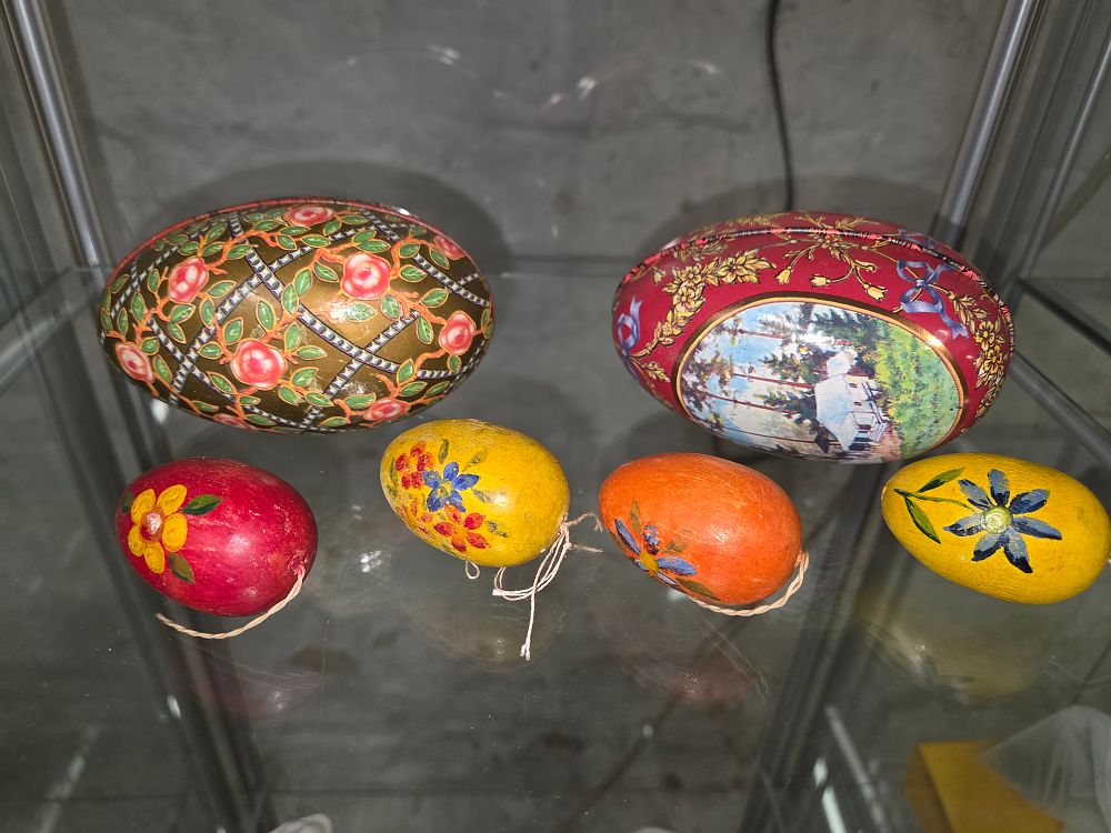 Lot 615 – A collection of decorative egg-shaped items comprising two lithographed metal candy tins by Chambers Candy Co and several smaller hand-painted floral eggs.