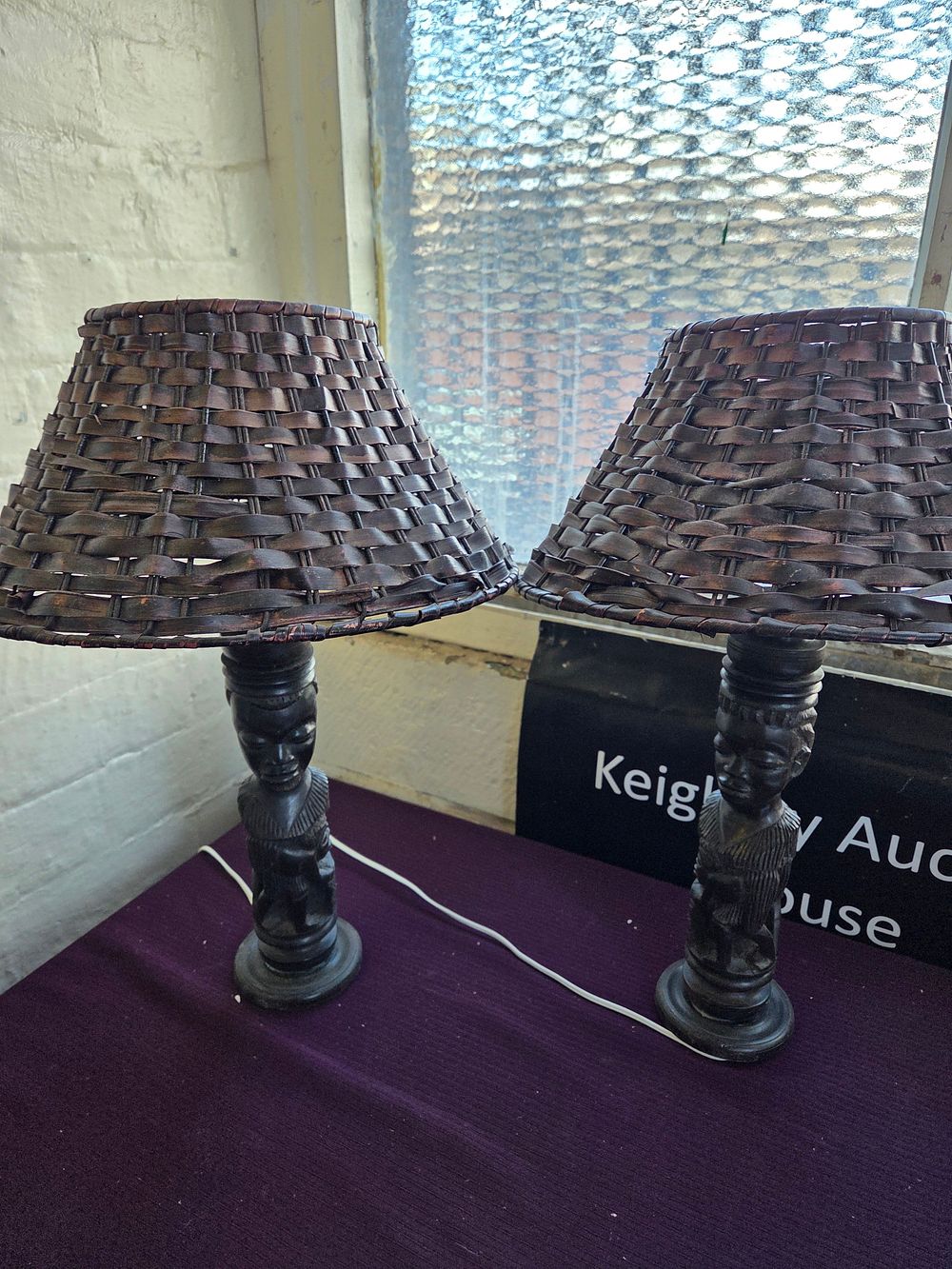 Lot 650 – A Pair of Mid-20th-Century Carved African Hardwood Table Lamps with Woven Wicker Shades