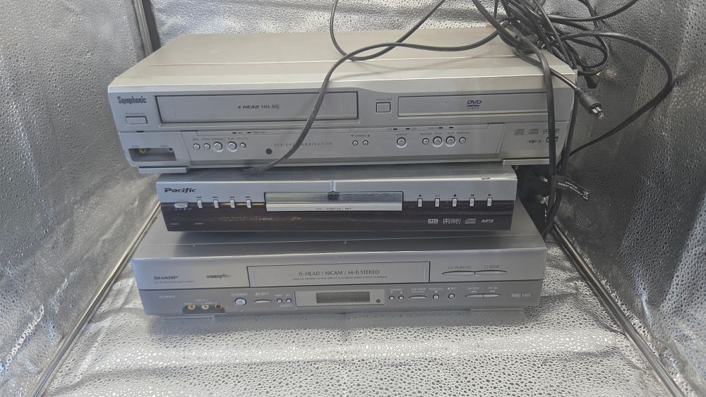 Lot 291 – A Trio of Silver-Coloured Home Media Devices Including Symphonic VCR/DVD Combo, Pacific DVD Player, and Sharp VCR Model VC-MH815. All Power up