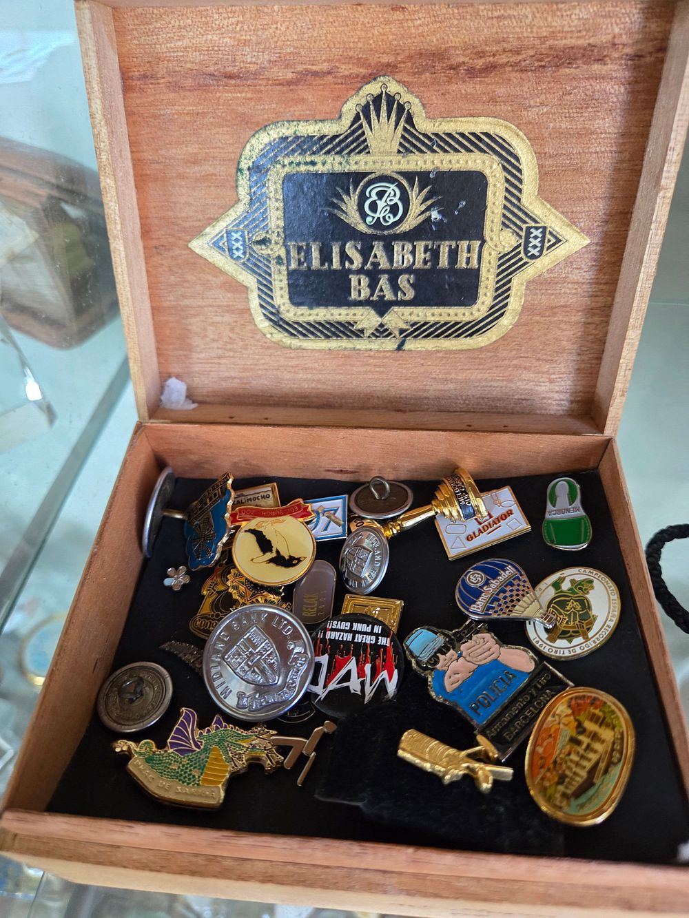Lot 653 – An Assortment of Late 20th Century Enamel and Metal Lapel Pins and Badges in an Elisabeth Bas Wooden Box