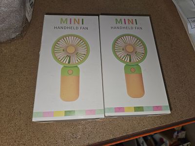 A Pair of Mini Handheld Portable Cooling Fans in Original Retail Packaging