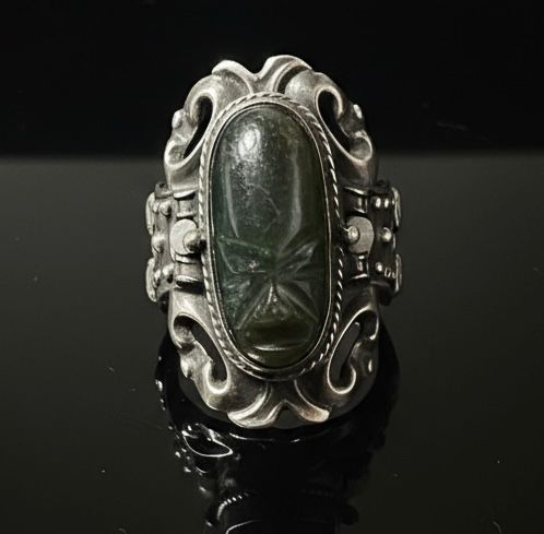 Lot 250: A GREEN STONE IN AN ADJUSTABLE SILVER RING DEPICTING A FACE