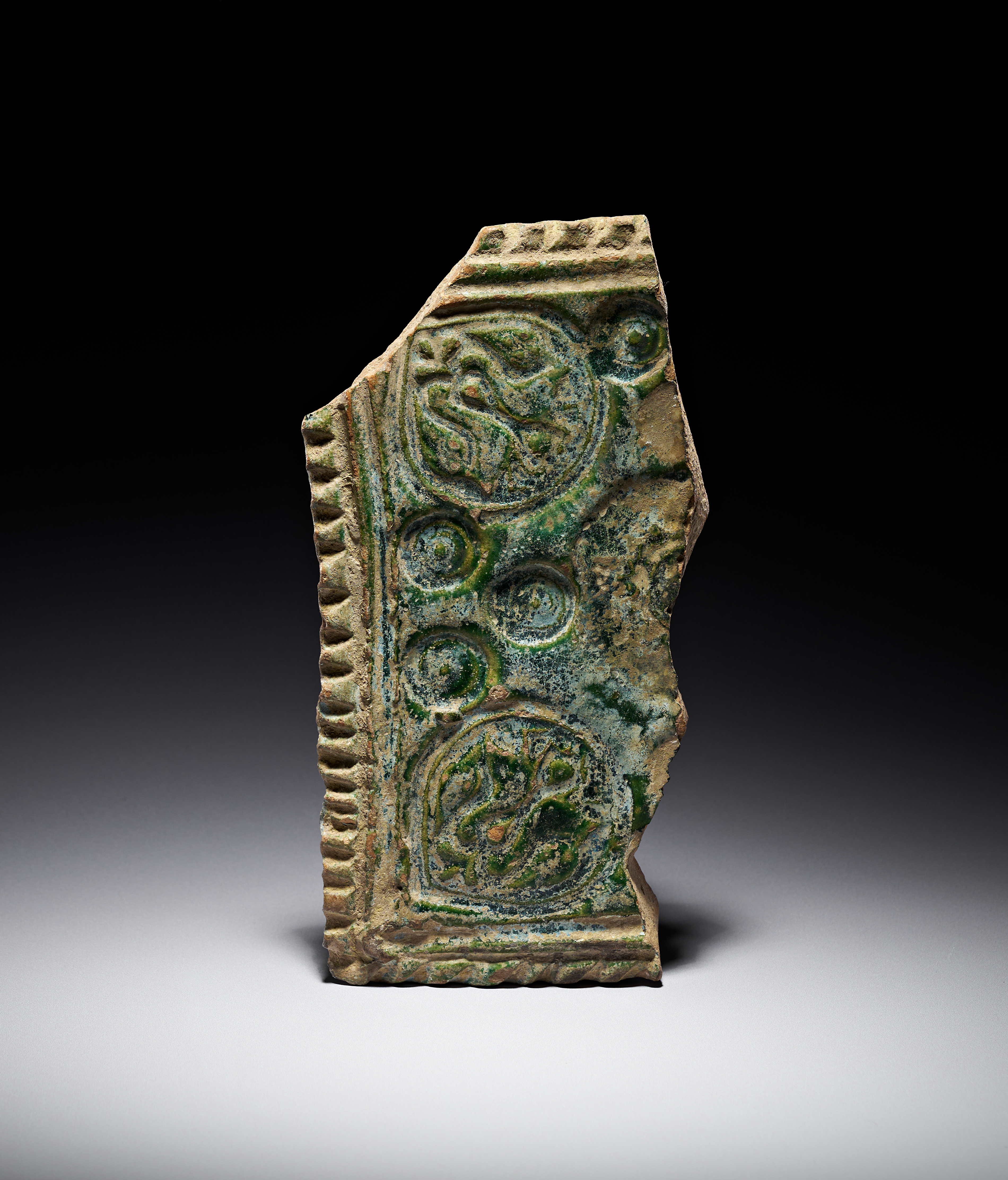 A RARE UMAYYAD MOULDED GREEN-GLAZED CERAMIC TILE FRAGMENT, EASTERN MEDITERRANEAN, 8TH CENTURY