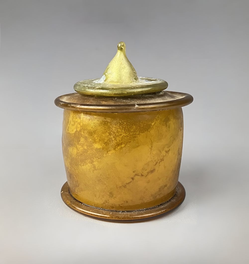 Lot 170: AN UMAYYAD OR EARLY ABBASID AMBER GLASS PYXIS WITH CONICAL LID/ INKWELL, MESOPOTAMIA, 8TH/ 9TH CENTURY