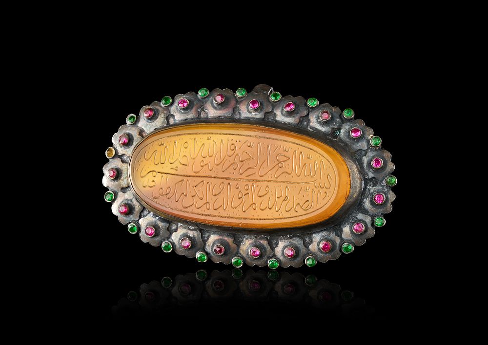 Lot 280: AN INDO-PERSIAN SILVER-MOUNTED CARNELIAN TALISMAN PENDANT WITH RED AND GREEN GEMSTONE BORDER, 19TH CENTURY