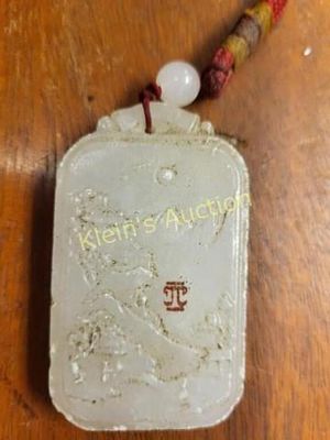 carved white jade pendant attached to a red cord. 2" x 1 1/2" carved scene with an attached bead 