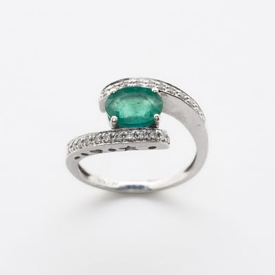 Sortija dise&ntilde;o cruzado en oro blanco con esmeralda central talla oval y brazos de pav&eacute; de 