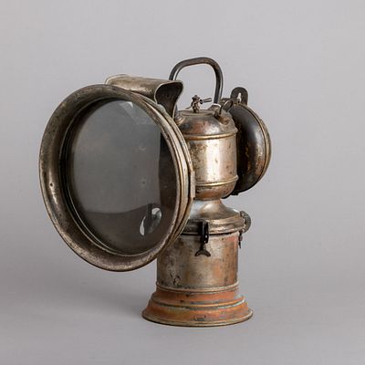 LANTERNA DE CARBURETO. Em diferentes metais, lente em vidro. Sinais de uso, amolgadelas e 