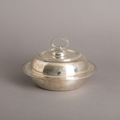 PRATO COBERTO. Em metal prateado, decoração lisa com frisos relevados. Sinais de uso. Dim.: 16x24 cm.