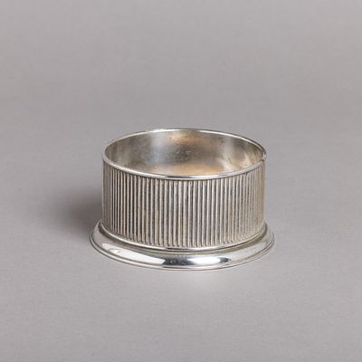 BASE PARA GARRAFA. Em metal prateado e base em corti&ccedil;a, decora&ccedil;&atilde;o relevada "caneluras". Sinais 