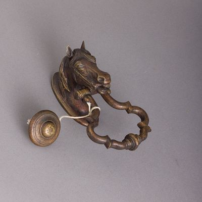 BATENTE DE PORTA. Em metal amarelo patinado, decora&ccedil;&atilde;o relevada "cabe&ccedil;a de cavalo". Sinais de 