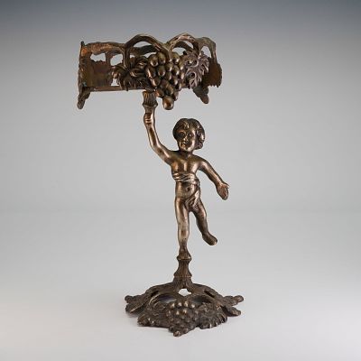 Bronze Putto Candle Holder. The object is constructed of bronzed metal and features a nude putto 
