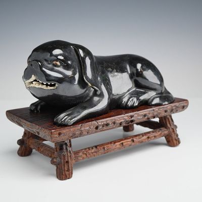 Black Glazed Porcelain Figurine of a Reclining Pug with Carved Wooden Stand. A black glazed 